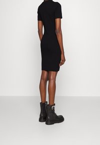 Svart figurnära klänning med korta ärmar, tillverkad av ett andningsbart material. I kombination med svarta ankellånga stövlar med dekorativ hårdvara.