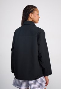 Zwarte jacket met een kraagontwerp, losse pasvorm en zichtbare zijzakken. Gemaakt van gladde stof en heeft een eenvoudige en schone uitstraling.