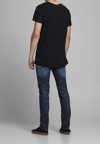 Camiseta negra de manga corta con escote redondeado, combinada con vaqueros azul oscuro que presentan acentos descoloridos y un corte estándar, llevada con zapatos negros.
