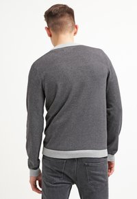 Grauer Pullover mit rundem Ausschnitt und hellgrauem, geripptem Kragen sowie Bündchen. Der Stoff wirkt weich und gestrickt, mit einer schlichten Textur.
