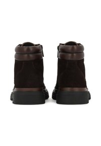 Botines de ante marrón con un cuello de cuero liso, cremalleras laterales y suelas de goma texturizada. Se puede ver un detalle de costura en contraste.