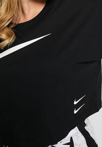 Svart kortärmad t-shirt i bomull med rund hals, prydd med stora vita swoosh-loggor över bröstet och en mindre logga vid fållen.