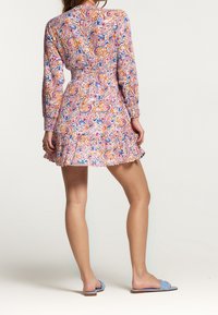 Vestido de manga larga con un diseño de paisley multicolor, cintura ajustada y falda acampanada con dobladillo con volantes. Combinado con sandalias de dedo azules.