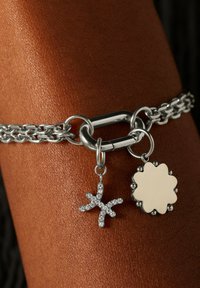Zilveren schakelarmband met grote schakels, voorzien van een stervormige hanger met strass-steentjes en een bloemvormige pendent met een gladde oppervlakte.