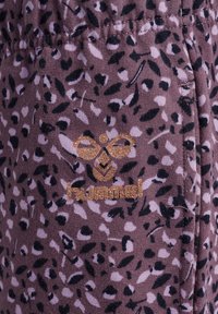 Leopardmönstrat tyg i nyanser av mauve och svart med en glänsande guldig "hummel"-logotyp. Mjuk textur, med en åtsittande passform och sydda detaljer.