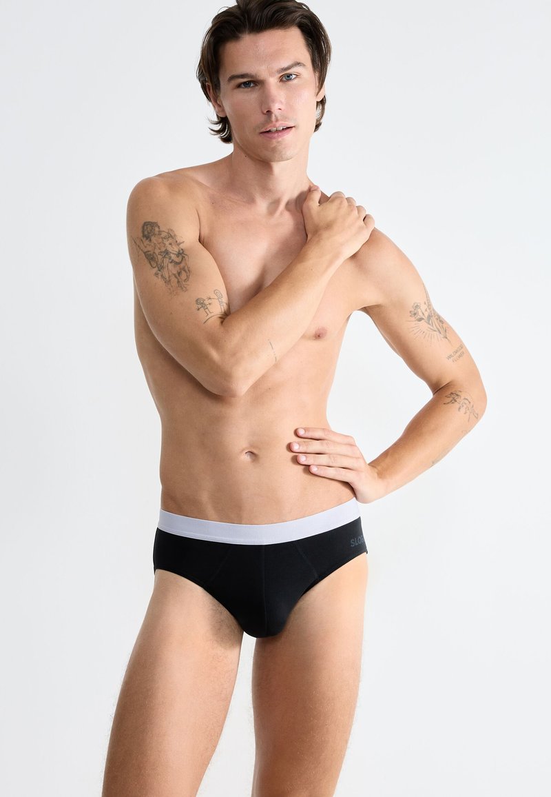 L'intimo corto nero con una fascia elastica bianca, caratterizzato da una texture liscia e un design aderente. La fascia presenta un dettaglio con logo.