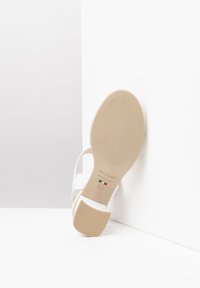White sandal with strap design, flat sole, and textured beige rubber bottom. "NeroGiardini" branding and Italian flag detail visible. Size 37.