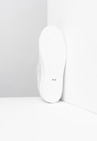 Bílé tenisky s texturovaným šedým svrškem, gumovou podrážkou s propracovanými vzory a malým detailem italské vlajky po straně.