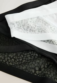 Bralette en maille noire et blanche avec un bord contrastant. Présente un motif délicat semblable à de la dentelle et un tissu lisse dans un design superposé.