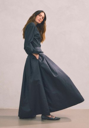 Long black dress with a fitted bodice, long sleeves, and a flowing skirt. Made from a smooth fabric; features side pockets and subtle shine.