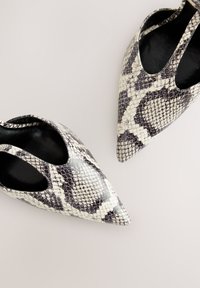 Chaussures à bout pointu avec un motif de peau de serpent noir et blanc, présentant des côtés découpés et une texture de surface lisse. Doublure intérieure noire.