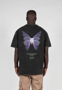 Black cotton t-shirt featuring a purple butterfly graphic on the back, with text below in white. Short sleeves and a relaxed fit design.