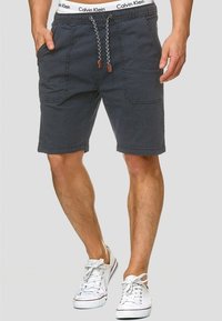 Shorts gris foncé avec une taille à cordon, dotés de poches avant et du logo Calvin Klein sur la ceinture. Portés avec des baskets blanches.