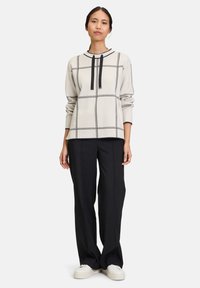 Light gray sweater with black grid pattern, featuring a round neckline and two black ties. Paired with black wide-leg trousers and white sneakers.