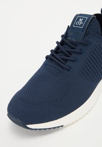 Navy athletic shoe featuring a textured knit upper, round toe, and white sole. Includes dark laces and a branded tongue label.