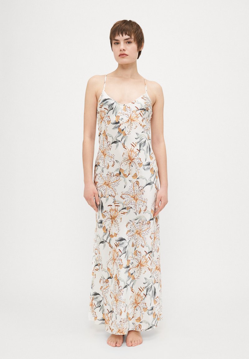 Maxi dress in soft white fabric featuring a floral pattern in orange and green. Spaghetti straps and a fitted bodice with a flowing skirt.