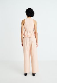 Top peplum en color durazno combinado con pantalones de pierna ancha. La parte superior presenta un diseño de volantes en capas; la tela tiene una textura suave. Calzado negro.