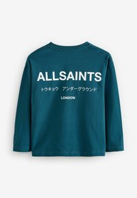 Tirkizna majica dugih rukava od pamuka, s bijelim natpisom: "ALLSAINTS," te dodatnim japanskim znakovima i "LONDON" na dnu.