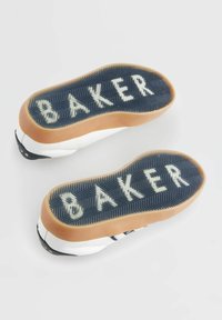 Chaussures de skate noires et blanches avec semelles en caoutchouc. La semelle extérieure présente un motif surélevé avec le logo "BAKER" en blanc. Conçues pour la durabilité et l'adhérence.