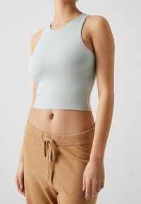 Woman wearing a fitted light gray sleeveless crop top and high-waisted tan drawstring pants against a plain background.