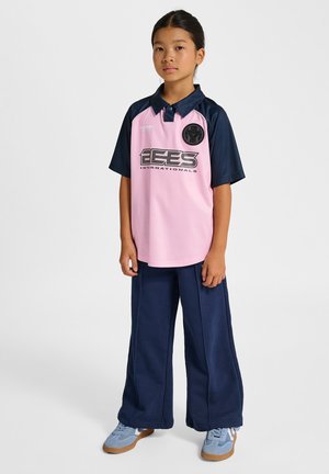 Korte mouw polo in roze met marineblauwe mouwen, met een logo op de borst en brede marineblauwe broek. Lichtblauwe sportschoenen.