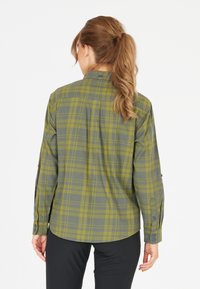 Grön rutigt skjorta med långa ärmar, knäppta manschetter och en rundad nederkant. Tillverkad av mjukt tyg, med ett distinkt rutmönster i subtila färger.