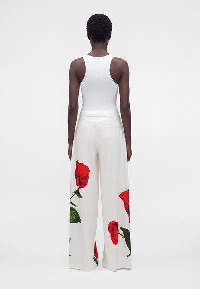 Personne vue de dos portant un haut blanc sans manches et un pantalon blanc à jambes larges avec de grandes impressions de fleurs rouges près du bas.