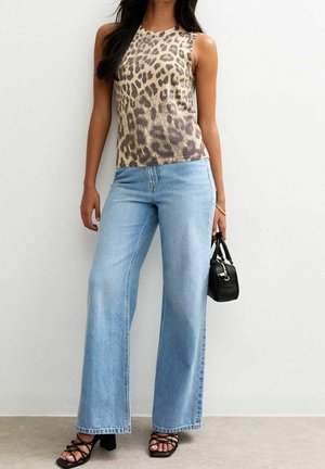 Kobieta ubrana w bezrękawnik w panterkę, jasnoniebieskie szerokie dżinsy, czarne sandały na obcasie z paskami, trzymająca małą czarną torebkę.