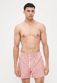 Shorts de bain rayés rouges et blancs avec une taille élastique, fabriqués en tissu léger, dotés d'une coupe amplement et d'une longueur jusqu'à mi-cuisse.