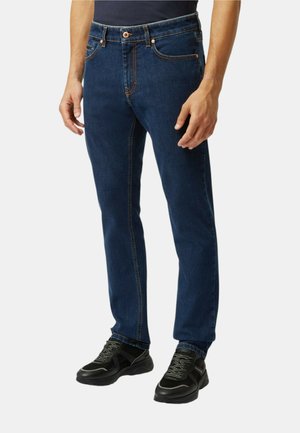 Jeans in denim blu scuro con vestibilità dritta, cuciture in vista, cinque tasche e chiusura con bottone anteriore. Indossati con scarpe sportive nere.
