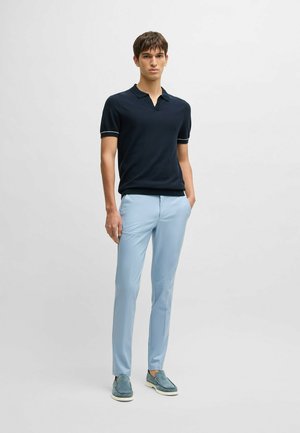 Navy polo shirt with short sleeves and a v-neck, paired with light blue tailored trousers and blue slip-on shoes. Simple and modern design.
