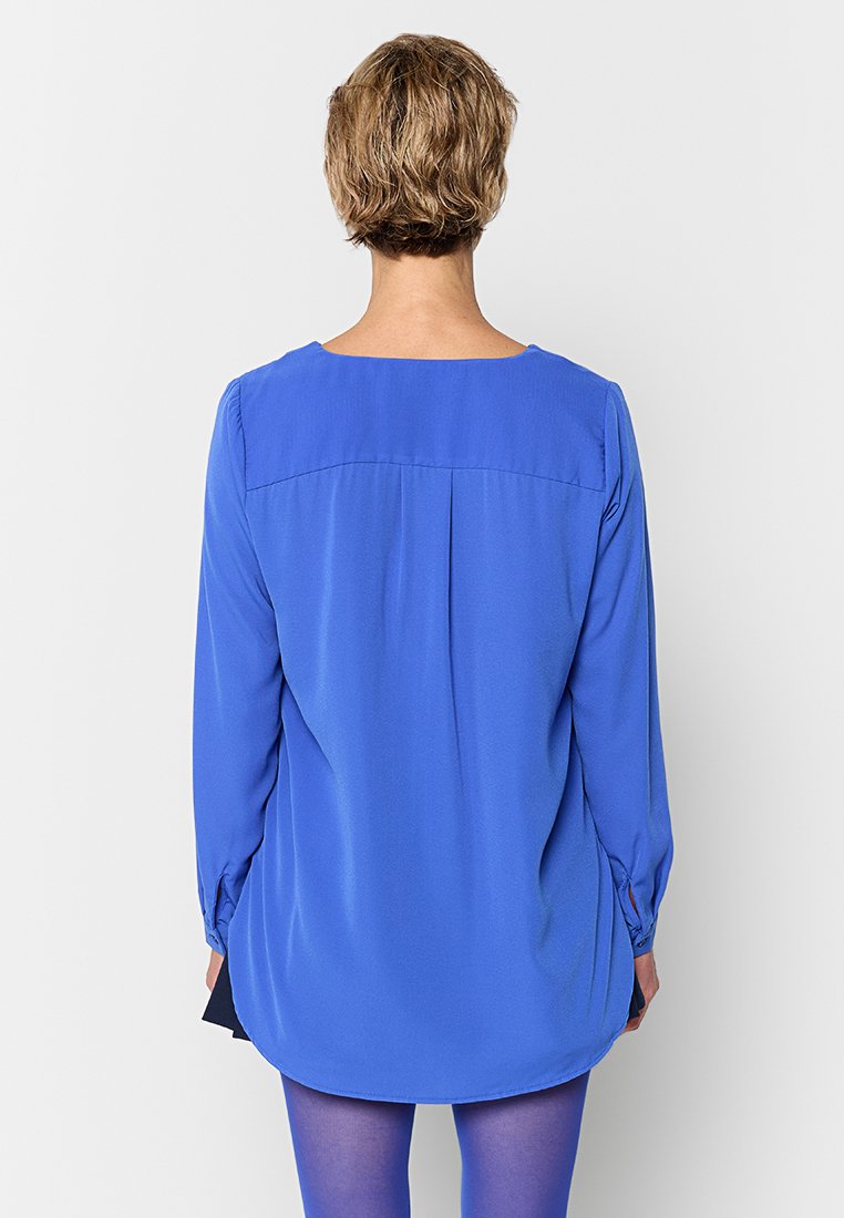Langärmlige, einfarbige blaue Bluse mit rundem Halsausschnitt, lockerer Passform und Faltendetail am Rücken, aus leichtem Stoff gefertigt.