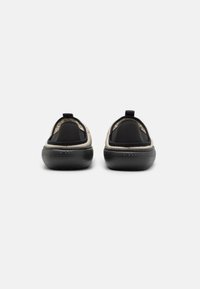 Svarta och beige slip-on skor med en strukturerad svart sula, utrustade med en vadderad krage och en dragrem bak för enkel påtagning.