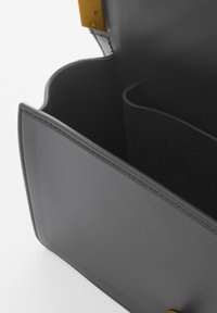 Grijze leren handtas interieur met een gladde textuur, voorzien van een gele hardwareaccent en een ontwerp met één compartiment.