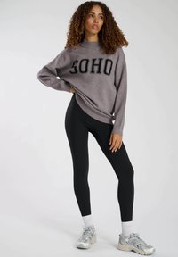 Grå oversized sweatshirt med "SOHO" i svart text, parat med svarta leggings och grå sportskor. Slät tyg och figurnära design.