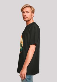 Schwarzes Baumwoll-T-Shirt mit lockerer Passform. Zeigt ein lebendiges, von der Natur inspiriertes Grafikdesign in Orange und Grün auf der Vorderseite. Einfaches Design, kurze Ärmel.