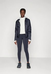 Tumesinine kerge jope kapuutsiga, valge pikemate varrukatega särk ja tumedad retuusid; kombineeritud mustade spordijalatsitega. Lihtne disain, ilma nähtavate mustriteta.