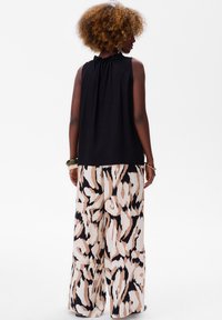 Czarna top bez rękawów z marszczonym dekoltem, w połączeniu z szerokimi spodniami w abstrakcyjny wzór w kolorze kremowym i czarnym.