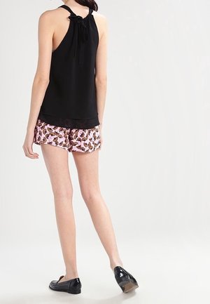 Zwarte mouwloze top met een strik aan de achterkant, gecombineerd met roze shorts met een vlinderpatroon. Draagt zwarte platte schoenen.
