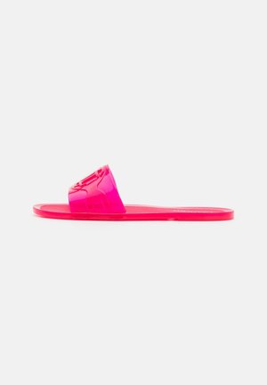 Mule translucide rose vif avec une large bride et une semelle plate sur un fond clair uni.