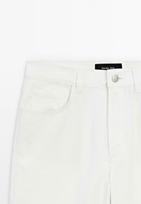 Vita bomullsbyxor med rak skärning, utrustade med en framficka, knappstängning och sydda detaljer. Märke synligt vid midjebandet.