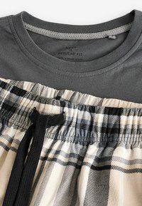Graues Baumwoll-T-Shirt mit einem Rundhalsausschnitt über beigen Karo-Shorts mit schwarzen Akzenten und Kordelzug. Reguläre Passform, weicher Stoff und lässiges Design.