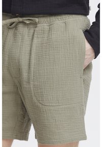 Olivgrüne Shorts aus strukturiertem, leichtem Stoff, mit elastischem Bund, Kordelzug und seitlichen Taschen.