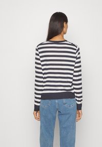 Gestreifter Pullover in Marineblau und Weiß, mit rundem Halsauschnitt, langen Ärmeln und geripptem Saum. Kombiniert mit blauen Jeans.