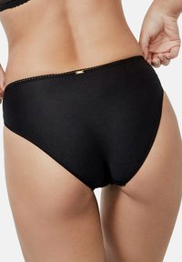 Culotte noire taille haute en tissu texturé, avec une bordure en dentelle sur le haut et un petit accent en métal doré à l'arrière pour le détail.