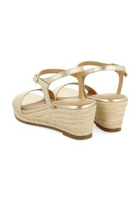 Sandales compensées dorées avec une semelle en espadrille texturée, des sangles croisées et un matériau supérieur lisse. Bride de cheville réglable avec détail de boucle.