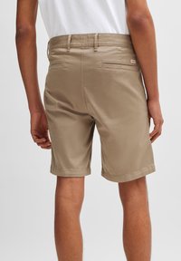 Shorts beiges à texture lisse, longueur genou, comportant quatre poches, des coutures visibles et un logo discret à l'arrière.