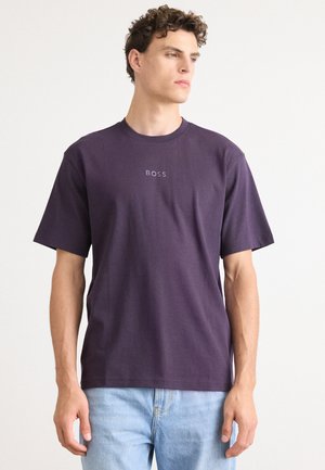 T-shirt en coton violet à manches courtes et col à ras du cou. Doté d'un logo central "BOSS" dans une teinte plus claire. Porté avec un jean léger bleu.