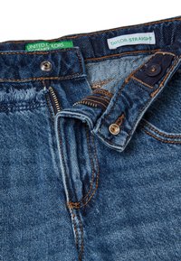 Jeans de mezclilla azul con corte recto, con costuras en tono marrón, cremallera y etiquetas de la marca en el interior de la cinturilla.