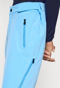 Lichtblauwe broek met meerdere ritssluitingen, een zachte textuur en een aansluitend ontwerp. Kenmerkt zich door een brede tailleband en contrasterende zwarte ritsen.